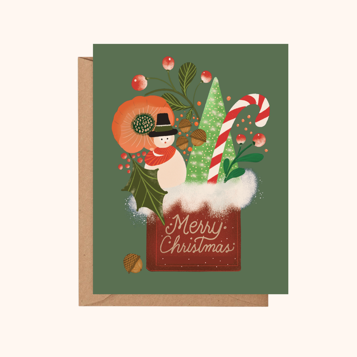 A Christmas greeting card with a dark green background and an illustrated winter scene, including a snowman, candy cane, holly, acorns, and the words 'Merry Christmas.' The card is shown with a kraft envelope behind it on a light beige background.